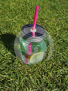 water with lemon in glass jar with pink straw on the green grass
