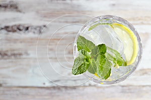 Water with lemon and mint in a glass container on a wooden table. place for text. refreshing summer citrus drink. vertical view of