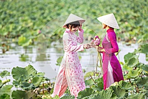 Water lilies on hand. Two Vietnamese woman is sitting on a wooden boat and collecting pink lotus flowers. Female boating on lakes