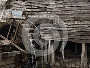 Water mill wheel rotates under a stream of water. Traditional village machinery