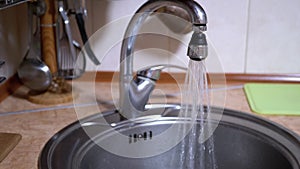 Water from An Open Nickel-Plated Faucet Flows into Sink in a Modern Kitchen