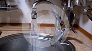 Water from An Open Nickel-Plated Faucet Flows into Sink in a Modern Kitchen