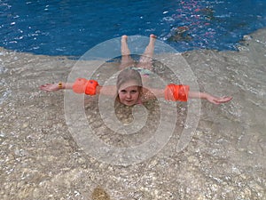 At the water Park, a girl in orange inflatable armbands lies in the pool.