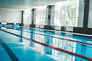A water pool with blue transparent clear water, on which bright sunlight shines. Water lanes in the swimming pool. indoor sports