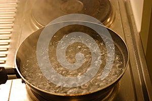 Water in the pot boils close up with steam above photo