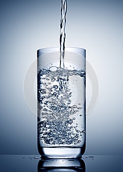 Water pour into glass with bubbles and reflection on blue grey