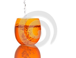 Water poured into beautiful orange colour glass - splashes. Isolated on white background.