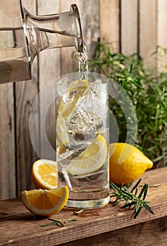 Water is poured from a decanter into a glass with ice and lemon slices