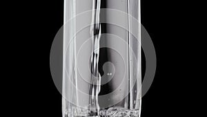 Water is poured into a faceted glass on a black background. Splashes and bubbles in the pure water. A glass of water to