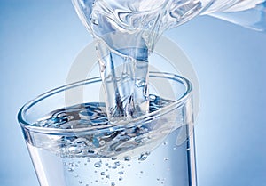 Water poured from jug into glass on blue background