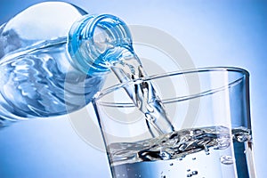 Water poured out of plastic bottle into glass isolated on blue background