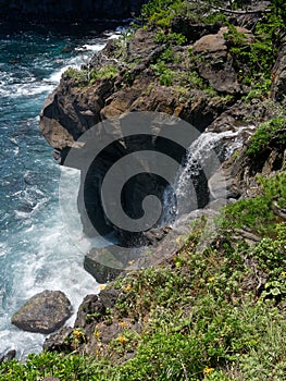 Water pouring down into the sea over the cliffs of the volcanic rocky coast