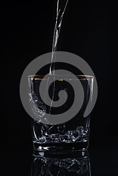 Water pouring into glass on dark background