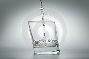 Water pouring into a glass on a gray background