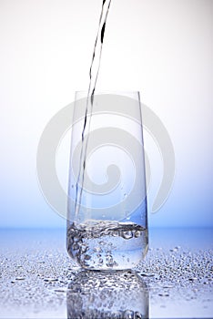 Water pouring into one-third full drinking glass on drops