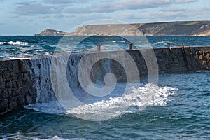 Water pouring over the harbour wall at Sennen, with a rainbow in the foreground