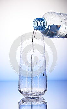 Water pouring from plastic bottle into empty drinking glass