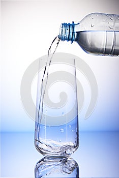 Water pouring from plastic bottle into empty drinking glass