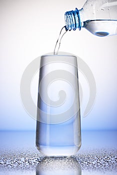 Water pouring from plastic bottle into full drinking glass