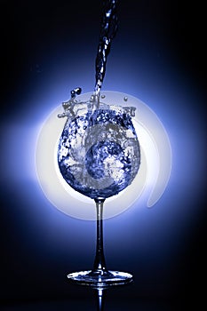 Water pouring into the wine glass on black reflective background, wine glass cup in which fresh water is poured