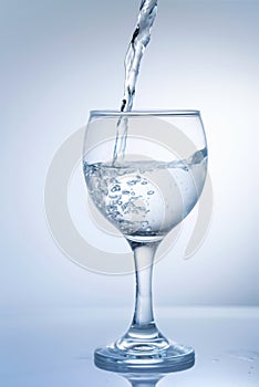 Water pouring into wine glass on a white background, close up