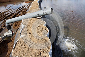 Water pump pumping flood water over sandbox barriers through large metal hose