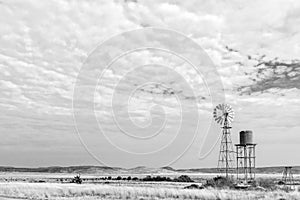 Water-pumping windmill and water tank on farm. Monochrome