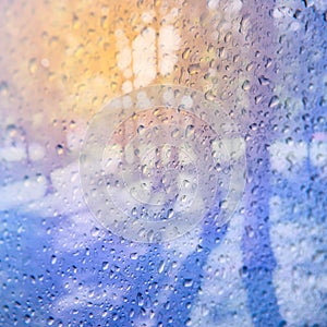 Water rain drops on blue glass surface as background. View on the park and sunlight through the wet window.