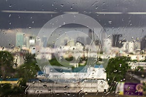 Water rain drops on window glass against blur image of building in bangkok city, Rainy day