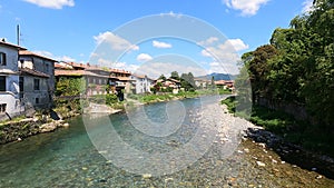 The water of a river flows fast between the houses under a blue sky