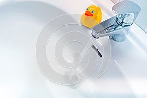 Water running from a faucet into a white sink with a rubber duck