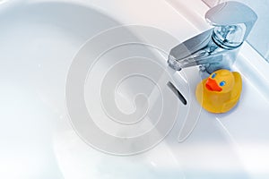 Water running from a faucet into a white sink with a rubber duck