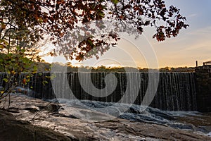 Water rushes over the edge of Yates Mill pond onto rocks in Raleigh, North Carolina at sunset in autumn