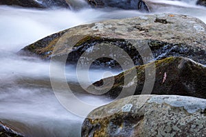 Water rushing around three large rocks in a cold mountain stream