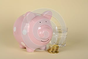 Water scarcity concept. Piggy bank, coins and glass of drink on beige background