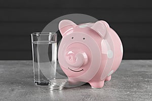 Water scarcity concept. Piggy bank, coins and glass of drink on grey table