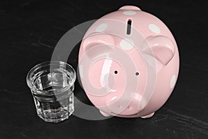 Water scarcity concept. Piggy bank and glass of drink on dark table