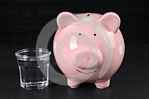 Water scarcity concept. Piggy bank and glass of drink on dark table