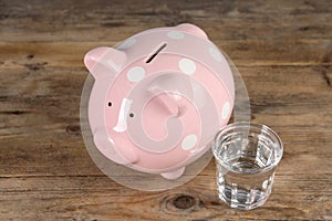 Water scarcity concept. Piggy bank and glass of drink on wooden table