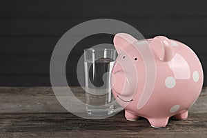 Water scarcity concept. Piggy bank and glass of drink on wooden table, space for text