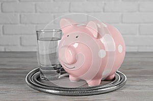 Water scarcity concept. Piggy bank, shower hose and glass of drink on wooden table