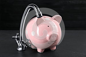 Water scarcity concept. Piggy bank and tap on dark table