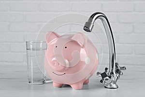 Water scarcity concept. Piggy bank, tap and glass of drink on white table