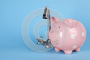 Water scarcity concept. Piggy bank and tap on light blue background, space for text