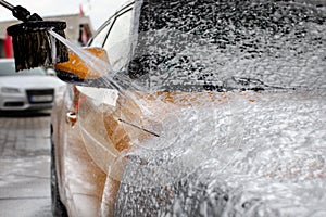 Water and shampoo stream falling on car covered with thick foam, when washed in carwash.