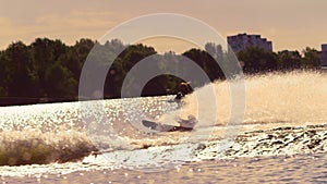 Water skier moving fast in splashes of water at sunset. Extreme watersports