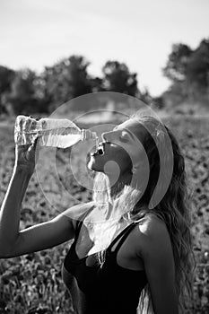 Water source. Fashionable woman posing. woman in field of poppy seed drink water from bottle