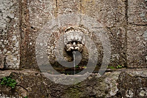 Water source in a stone wall. Ancient fountain with a face sculpture