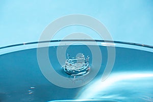 Water splash in crown shape and falling drop. Splash of the falling drops of water. Water drop on blue background. Blue water