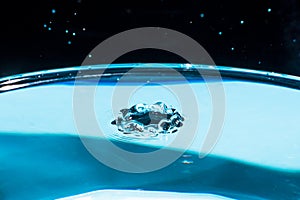 Water splash in crown shape and falling drop. Splash of the falling drops of water. Water drop on blue background. Blue water